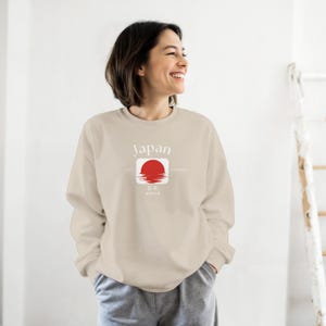 May include: Beige sweatshirt with the word "Japan" above a red sun graphic. The graphic includes Japanese characters and the words "est. since". The sweatshirt is a neutral color and has long sleeves.