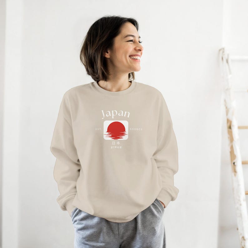May include: Beige sweatshirt with the word "Japan" above a red sun graphic. The graphic includes Japanese characters and the words "est. since". The sweatshirt is a neutral color and has long sleeves.