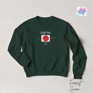 May include: Forrest Green sweatshirt with a graphic design featuring the word "Japan" above a red sun emblem. The design includes Japanese characters and the text "EST. 1980s". The sweatshirt is a solid color.
