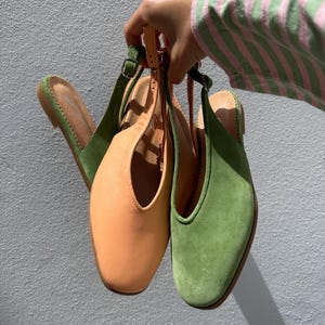 May include: Three pairs of women's slingback shoes in shades of green and peach. The shoes have a square toe design and adjustable straps. The shoes are held up against a light gray wall.
