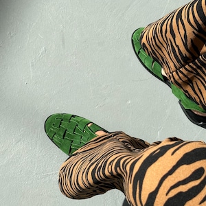 Puede incluir: Vista a&eacute;rea de sandalias verdes tejidas y pantalones con estampado de cebra marr&oacute;n y negro. Las sandalias tienen suela plana y dise&ntilde;o tejido. Los pantalones tienen un atrevido estampado de rayas de cebra.