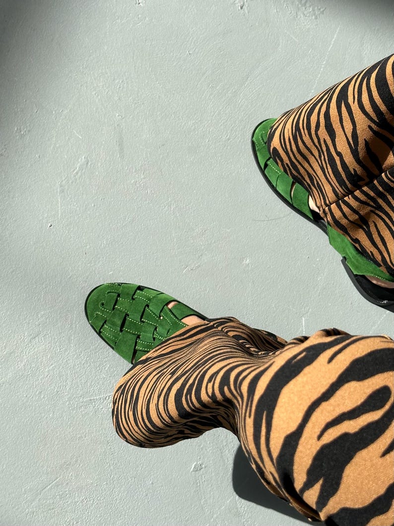 Puede incluir: Vista a&eacute;rea de sandalias verdes tejidas y pantalones con estampado de cebra marr&oacute;n y negro. Las sandalias tienen suela plana y dise&ntilde;o tejido. Los pantalones tienen un atrevido estampado de rayas de cebra.