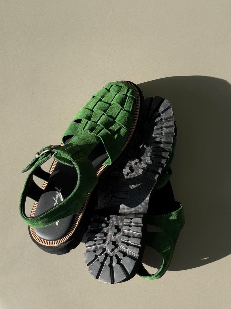 Puede incluir: Sandalias de ante verde con dise&ntilde;o superior tejido. Las sandalias tienen una suela negra con dibujo de tacos y cierre de hebilla. Las sandalias se muestran desde arriba.