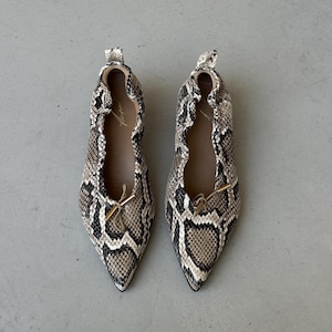 Puede incluir: Un par de zapatos planos de punta afilada con estampado de piel de serpiente en tonos beige, marrón, negro y blanco. Los zapatos tienen un borde elástico fruncido, una pequeña lengüeta en el talón y un lazo decorativo con puntas de metal dorado.