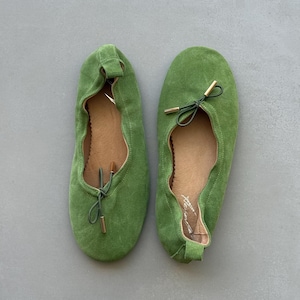 May include: A pair of grass green suede ballet flats featuring a rounded toe, a gathered elasticised topline, and a thin green drawstring cord tied in a bow at the front with metallic gold-toned aglets at the ends of the cord tips.