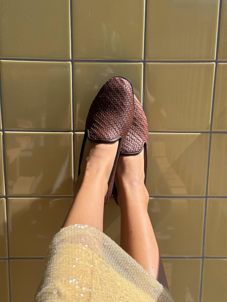 May include: Brown woven leather loafers with black trim. The shoes are displayed against a yellow tiled background. The loafers have a classic design, suitable for casual or semi-formal wear.