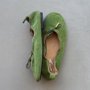 May include: A pair of bright green suede ballet flats featuring a rounded toe, a thin drawstring tie with gold-toned metal aglets at the front, a tan interior lining, and a small pull tab at the heel. The shoes have a flat black sole.