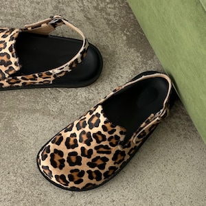 May include: Two pairs of footwear featuring a leopard print design. One is a sandal with a strap, and the other is a slip-on shoe. Both have black soles and a tan and brown spotted pattern.