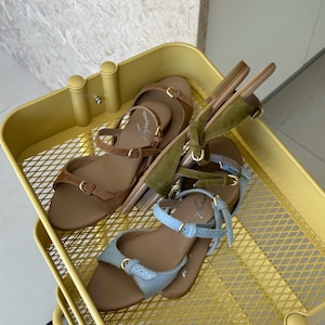 May include: Three pairs of sandals in a yellow metal cart. The sandals are in shades of brown, green, and light blue. Each pair has a strap and buckle closure. The cart has a diamond-shaped grid pattern.