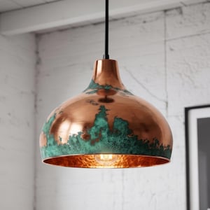 May include: A dome-shaped pendant light fixture featuring a polished copper exterior finish with a textured, oxidized green patina along the lower edge. The interior surface of the metal shade is hammered copper, and it hangs from a black cord.