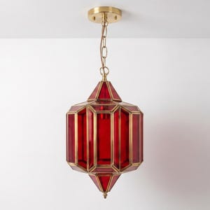 Könnte beinhalten: Eine hängende Pendelleuchte in sechseckiger Laternenform mit tiefroten Glasscheiben in einem Rahmen aus poliertem Messing, die an einer passenden Messing-Deckenrosette mit einer kurzen, dekorativen Messingkette befestigt ist.
