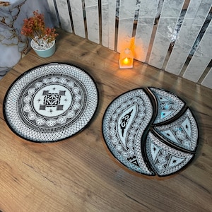 Peut inclure: Deux plats de service décoratifs noirs et blancs avec des motifs géométriques complexes. L'un est rond, l'autre est un plat à trois sections. Les plats sont sur une surface en bois, avec une petite plante et une bougie en arrière-plan.