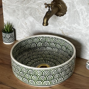 Peut inclure: Un lavabo rond en céramique avec un motif vert et blanc. Le lavabo est monté sur une surface en bois, avec un robinet en laiton et une petite plante décorative dans un pot à motifs assortis. Le diamètre du lavabo est d'environ 40 cm.