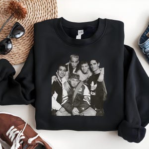 May include: Black crewneck sweatshirt featuring a black and white image of a boy band. The image shows six young men posing together. The sweatshirt is made of a soft material.