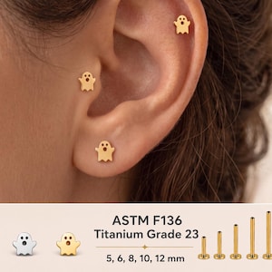 Puede incluir: Tres pendientes en forma de fantasma de color dorado se llevan en la oreja. El texto indica ASTM F136 Titanium Grade 23, 5, 6, 8, 10, 12 mm, con pendientes de fantasma plateados y dorados y cinco postes planos de distintas longitudes.