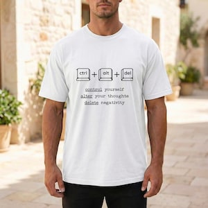 May include: White t-shirt with a black graphic featuring computer keyboard keys and the words "control yourself, alter your thoughts, delete negativity." The shirt is a crew neck style.