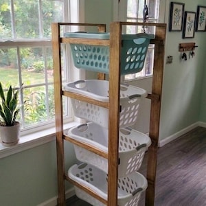 May include: A wooden laundry sorter with four white laundry baskets and two teal baskets. The sorter is made of stained wood and is placed near a window. The baskets are designed to hold laundry.