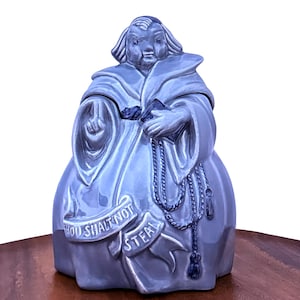 May include: A ceramic cookie jar in the shape of a robed figure, in a light blue-gray color. The figure holds a book and a rosary. A banner across the front reads "Thou Shalt Not Steal."