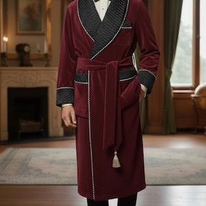 May include: A burgundy velvet robe with black quilted lapels and cuffs, trimmed with white piping. The robe features a matching belt and pockets, and a tassel. The garment is worn over a white shirt and black bow tie.