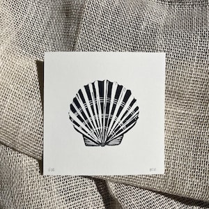 May include: A square white paper print featuring a black ink linocut illustration of a scallop shell. The shell is centered with detailed radial ridges. The bottom left corner is marked 1/0E and the bottom right corner is marked BCK in pencil.