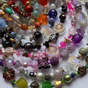 May include: A collection of colorful beaded necklaces with various shapes and sizes. The beads are in shades of red, orange, blue, purple, pink, green, and gold. Some beads have floral and starburst designs, and others are iridescent.