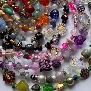 May include: A collection of multi-colored beaded necklaces featuring a variety of shapes, sizes, and textures. The beads include clear, opaque, metallic, and iridescent finishes in shades of pink, green, blue, orange, black, and purple.