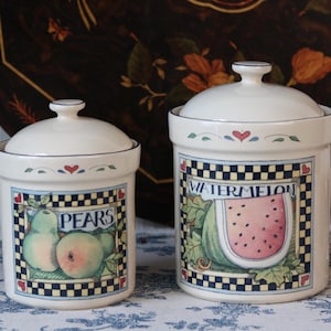 Op de afbeelding: Twee off-white keramische voorraadpotten met deksels, elk voorzien van een vierkante rand met een zwart-wit geblokt patroon. De kleinere pot toont het woord PEARS met twee peren, terwijl de grotere WATERMELON met een schijf watermeloen toont.