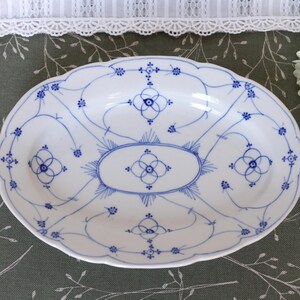 Pode incluir: Uma travessa de servir oval em porcelana com base branca e um delicado padrão floral pintado à mão em azul. O design apresenta linhas intrincadas interligadas, pequenas flores e motivos de raios de sol centrados na superfície.
