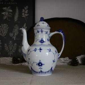 Può includere: Caffettiera in porcellana bianca con decoro floreale e a vite blu. La caffettiera ha un beccuccio curvo, un manico e un coperchio con un piccolo pomello. Il disegno si ripete sul coperchio, sul manico e sul corpo.