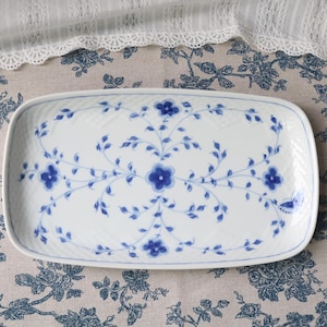 May include: A white ceramic mug with a black handle and the text "But First, Coffee" in a handwritten style. The mug is on a white surface. The mug is likely for hot beverages.