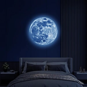 Puede incluir: Decoración mural de luna azul brillante, con cráteres detallados y un halo brillante. La luna está montada sobre una cama con ropa de cama y almohadas de color gris oscuro, creando un tema de dormitorio celestial.