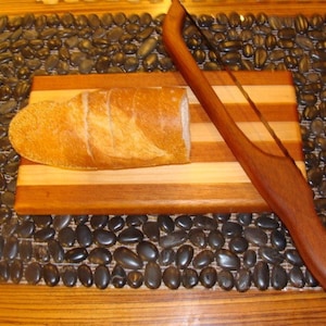 May include: A wooden bread board with a loaf of bread on top and a wooden bread knife with a serrated blade.