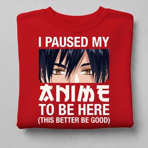 Puede incluir: Sudadera roja con texto blanco e ilustración estilo anime. El texto dice "I PAUSED MY ANIME TO BE HERE (THIS BETTER BE GOOD)". La ilustración presenta un primer plano de ojos y cabello de anime.