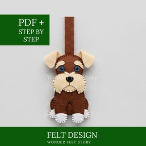 May include: A brown and cream felt dog ornament with blue button eyes, a black stitched nose, and white paw accents. The design includes a vertical felt strap at the top. Text on the image reads PDF + STEP BY STEP, FELT DESIGN, and WONDER FELT STORY.