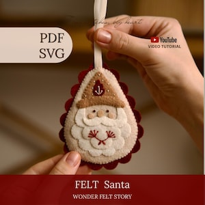 May include: A teardrop-shaped felt Santa ornament featuring a tan hat with a small anchor icon, a white beard with red embroidered details, and a scalloped dark red backing. The ornament includes a cream-colored ribbon loop for hanging.