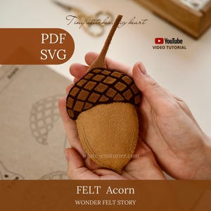 Könnte beinhalten: Ein handgefertigtes Eichel-Ornament aus Filz mit einem hellbraunen Nusskörper und einer dunkelbraunen, strukturierten Kappe mit Stiel. Das Bild enthält den Text PDF, SVG, Tiny stitches, big heart, YouTube VIDEO TUTORIAL, white-couturier.com, FELT Acorn und WONDER FELT STORY.