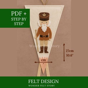 May include: A felt banner featuring a detailed design of a nutcracker soldier. The banner is cream-coloured with a brown and tan nutcracker figure. The banner is 27cm (10.6") tall. Text on the banner reads "PDF + STEP BY STEP" and "FELT DESIGN".