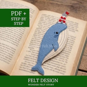 Könnte beinhalten: Blaues Filz-Wal-Lesezeichen mit Leuchtturm-Hut, auf einem offenen Buch. Das Lesezeichen hat ein genähtes Design und den Text "Wonder Felt Story". Das Bild enthält auch den Text "PDF + STEP BY STEP" und "FELT DESIGN".