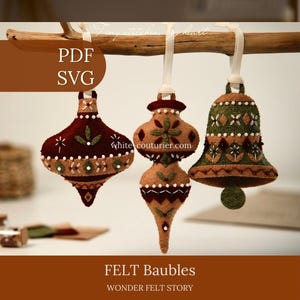 May include: Three hanging felt ornaments in maroon, tan, and olive green, featuring intricate embroidery and white ribbon loops. The ornaments are shaped like a pointed bauble, a double-tiered bauble, and a bell. Text reads PDF, SVG, white-couturier.com, FELT Baubles, WONDER FELT STORY.