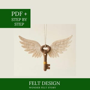 May include: A felt key with cream-colored wings, suspended by a string. The key is brown with a gold-colored accent. The image includes the text "PDF + STEP BY STEP" and "FELT DESIGN WONDER FELT STORY".