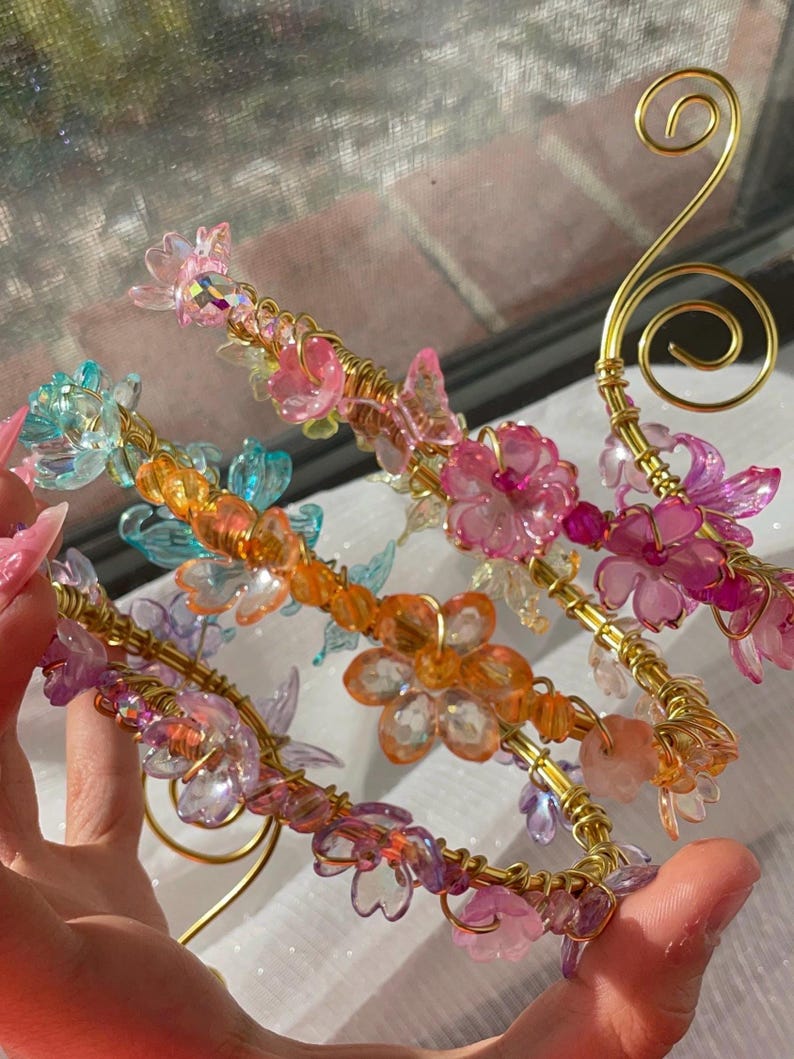 May include: Close-up of several decorative hair accessories. Each accessory features a gold wire base adorned with colorful, translucent flowers and beads in shades of pink, orange, blue, and purple. The design includes a swirl detail.