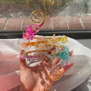 May include: A decorative gold-colored wire sculpture with four tiers of colorful, translucent butterfly accents. The butterflies are pink, yellow, purple, and teal. The sculpture has a swirling design.