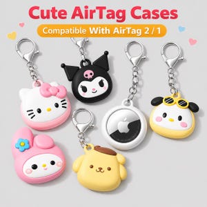 Könnte beinhalten: Eine Sammlung von Silikon-AirTag-Hüllen mit verschiedenen Cartoon-Charakter-Designs, darunter eine weiße Katze, eine schwarze Figur mit Totenkopf, ein gelber Hund und ein rosa Hase. Jede Hülle enthält einen silbernen Karabiner-Schlüsselanhänger.