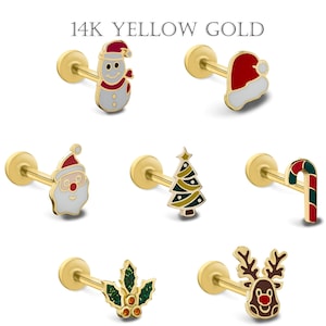 Puede incluir: Pendientes de botón navideños de oro amarillo de 14K. Los diseños incluyen un muñeco de nieve, gorro de Papá Noel, cara de Papá Noel, árbol de Navidad, bastón de caramelo, hojas de acebo y un reno. El texto "14K YELLOW GOLD" está en la parte superior.