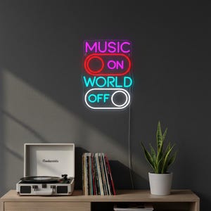 Può includere: Un'insegna al neon con le parole "MUSIC ON WORLD OFF" in rosa, rosso e blu. L'insegna è montata su una parete grigio scuro. Un giradischi bianco e una pila di dischi in vinile sono su una superficie di legno.