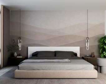May include: A modern bedroom featuring a bed with a beige base and gray bedding. The headboard is white, and the wall behind the bed has a layered, abstract design in shades of brown. Two pendant lights hang above the bed.