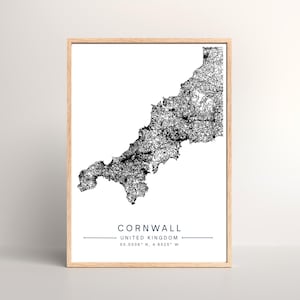 May include: A framed print featuring a detailed black and white map of Cornwall, United Kingdom. The print includes the name "Cornwall" and geographical coordinates. The frame is a light wood color, and the print is on a white background.