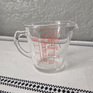 May include: A clear Pyrex measuring cup with a handle and a pouring spout. Red markings indicate measurements in ounces and cups. The cup is designed for kitchen use.