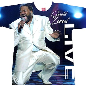 May include: White t-shirt featuring a vibrant image of Gerald Levert performing live on stage. The design includes the singer in a white suit, a microphone, and the word "LIVE" in bold white letters. The shirt is a music-themed apparel item.