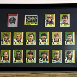 May include: A black framed display featuring a collection of vintage Newcastle United football trading cards. The arrangement includes a team logo card, a team photo, and individual player portraits with names printed below each image.